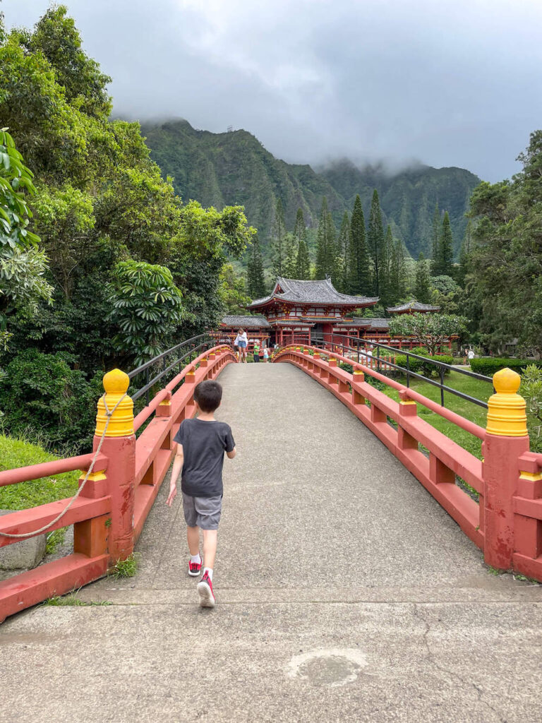 Image of a boy walking across a bridge to a red temple on Oahu