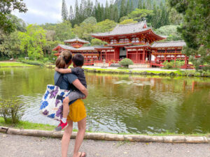 Check out this guide to Byodo In Temple on Oahu by top Hawaii blog Hawaii Travel with Kids. Image of a mom and son looking at a red temple in Hawaii