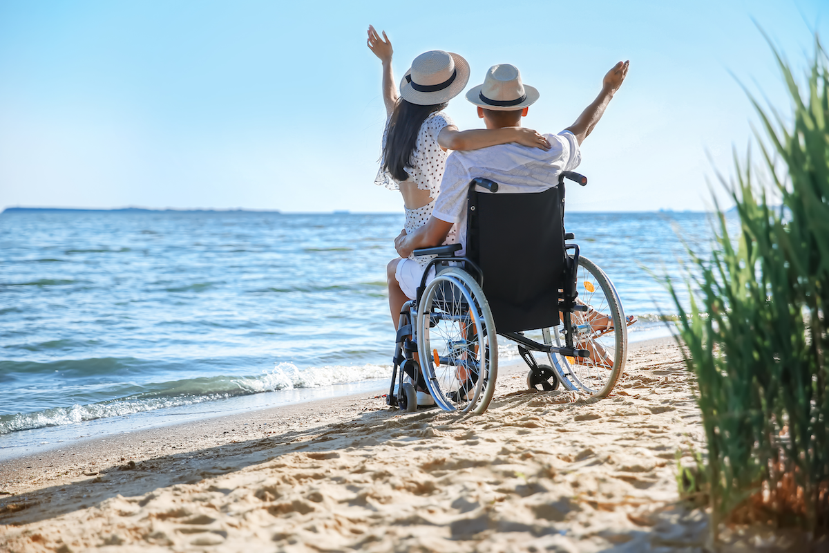 Find out the best Hawaiian island for wheelchair users. Image of a couple in a wheelchair on a beach