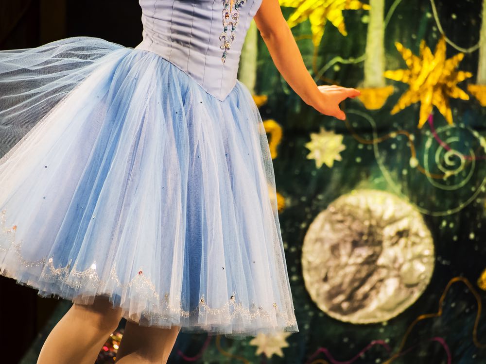 Image of a ballet dancer in a blue tutu in front of a Christmas tree prop on The Nutcracker stage