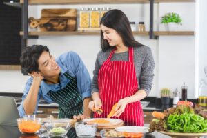 Find out the best Hawaii Christmas gifts for foodies recommended by top Hawaii blog Hawaii Travel with Kids! Image of Close up shot of Asian couple in apron, man make eye contact with woman that grates the carrot into strips, in kitchen, concept for happy lover.