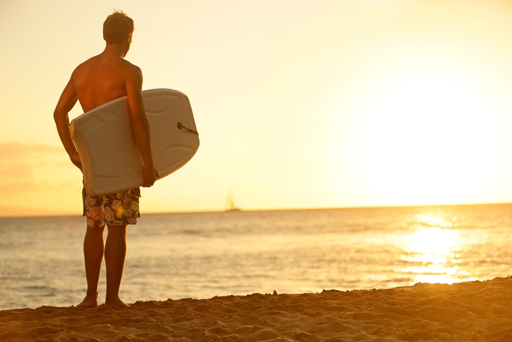 Surfer man on beach at sunset holding bodyboard. Fit male body surfer guy enjoying sunset and bodyboarding on summer holidays vacation on tropical beach. Fitness model, Kaanapali beach, Maui, Hawaii.