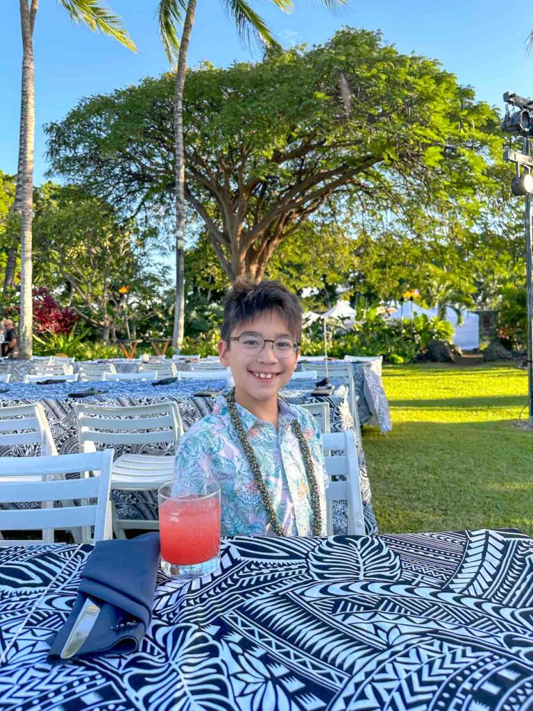 Image of a boy wearing an Aloha shirt sitting at a luau table in Hawaii