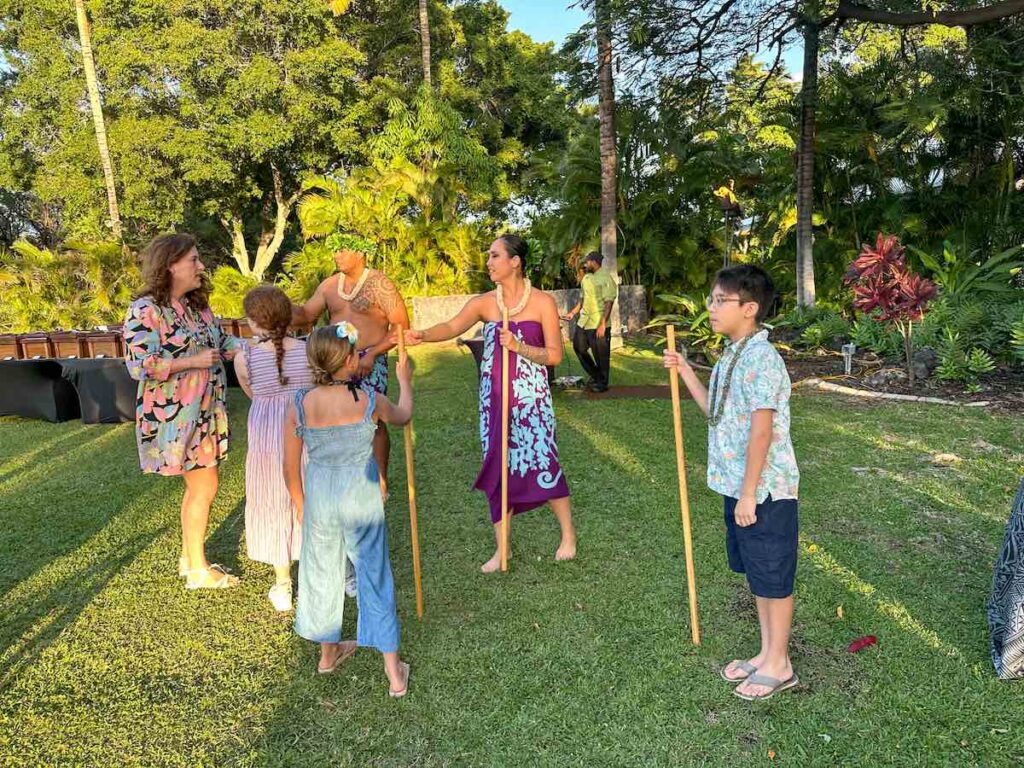 Image of kids holding large sticks playing a game at a Hawaiian luau