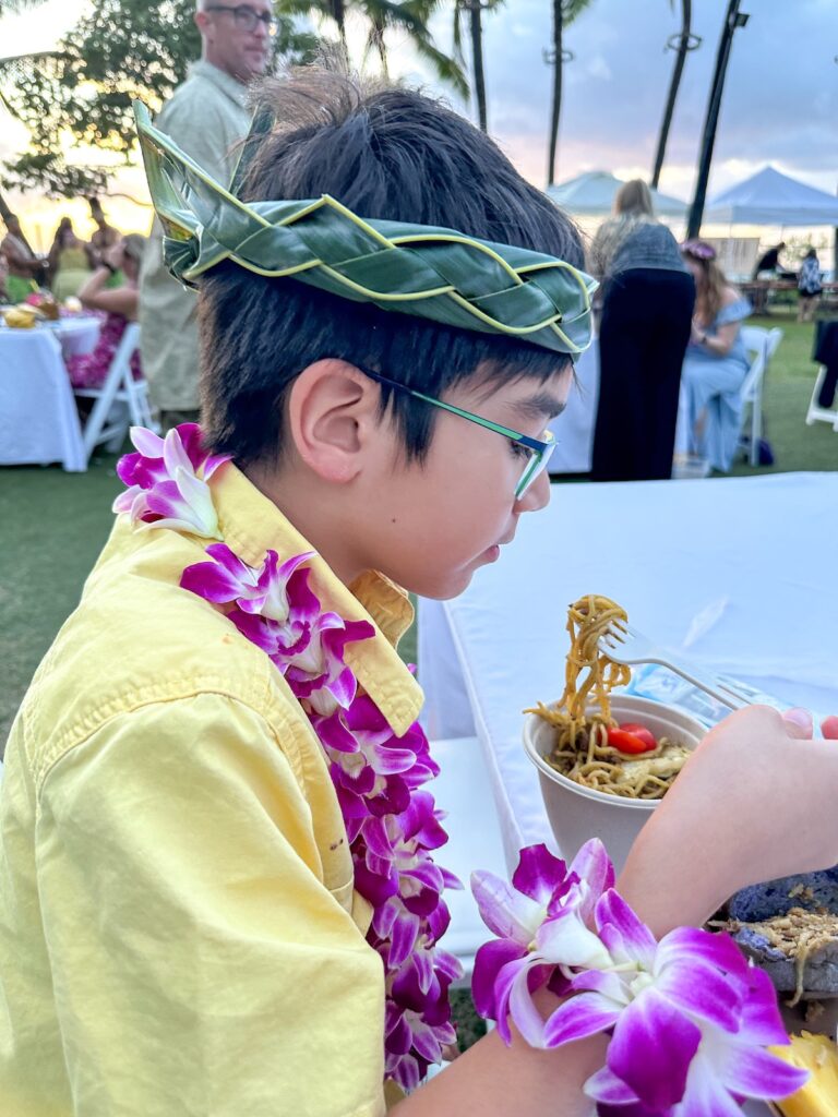 Image of a boy eating noodles at the Diamond Head Luau on Oahu. Photo credit: Marcie Cheung of Hawaii Travel with Kids