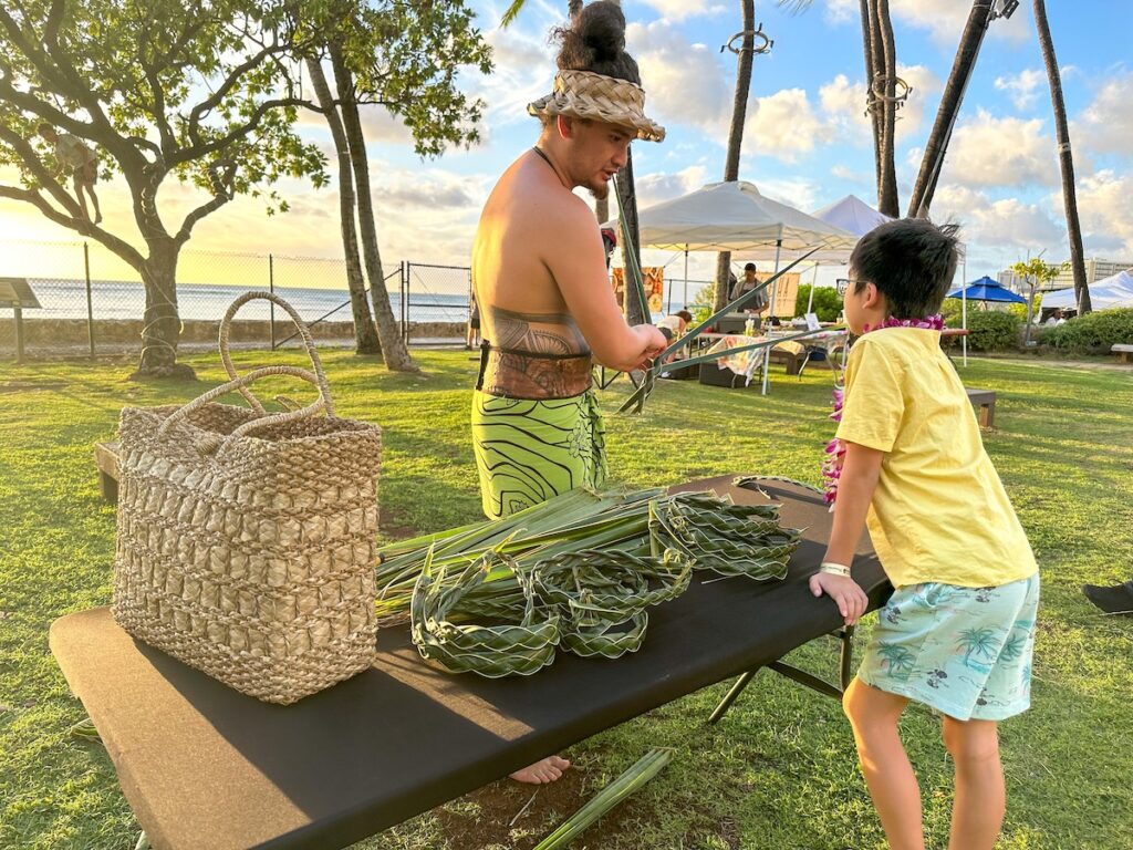 Image of a boy learning how to weave a coconut front headband at the Diamond Head Luau on Oahu. Photo credit: Marcie Cheung of Hawaii Travel with Kids