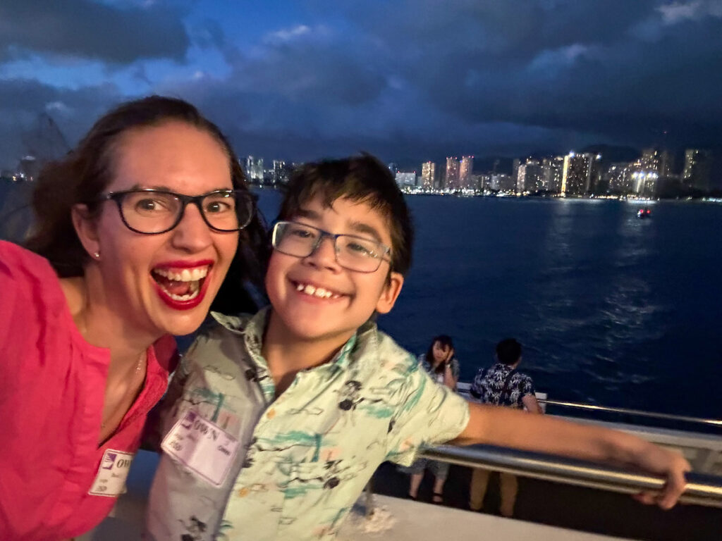 Image of Marcie Cheung and her son on the deck of the Star of Honolulu at night with Waikiki lights in the background. Photo credit: Marcie Cheung