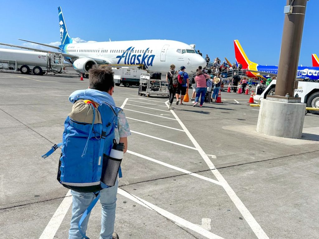 Find out how to fly to Hawaii with kids without losing your mind with tips from top Hawaii travel blog Hawaii Travel with Kids. Image of a boy walking toward a plane in Hawaii