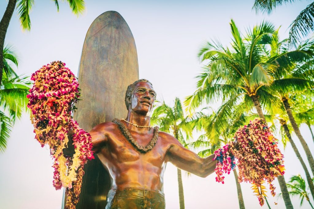 Find out the biggest Oahu mistakes tourists make and get Oahu travel tips from top Hawaii blog Hawaii Travel with Kids. Image of Hawaii travel destination. Duke Kahanamoku statue with leis in Waikiki beach in Honolulu city , Oahu, USA summer vacation.