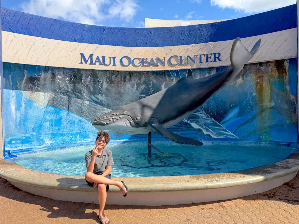 Check out this honest Maui Ocean Center review by top Hawaii travel expert Marcie Cheung. Image of a boy in front of a Maui Ocean Center sign.