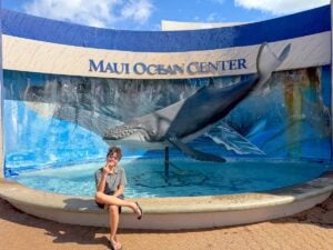 Check out this honest Maui Ocean Center review by top Hawaii travel expert Marcie Cheung. Image of a boy in front of a Maui Ocean Center sign.